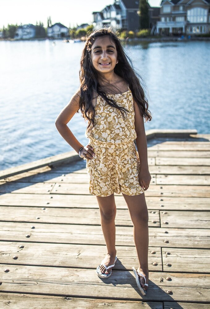 A little girl standing by a lake in a yellow floral dress with her hand on her hip