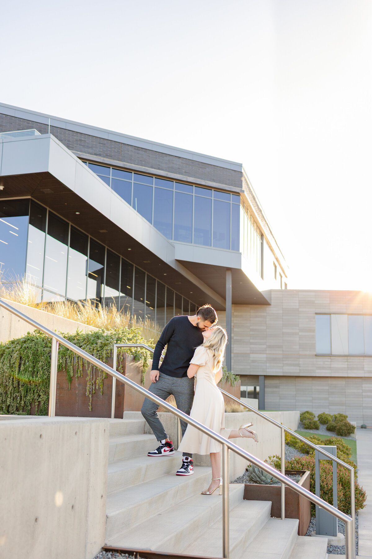 Stunning photo of the man bending to kiss his fiance on the steps of a local college with the sun shining behind them