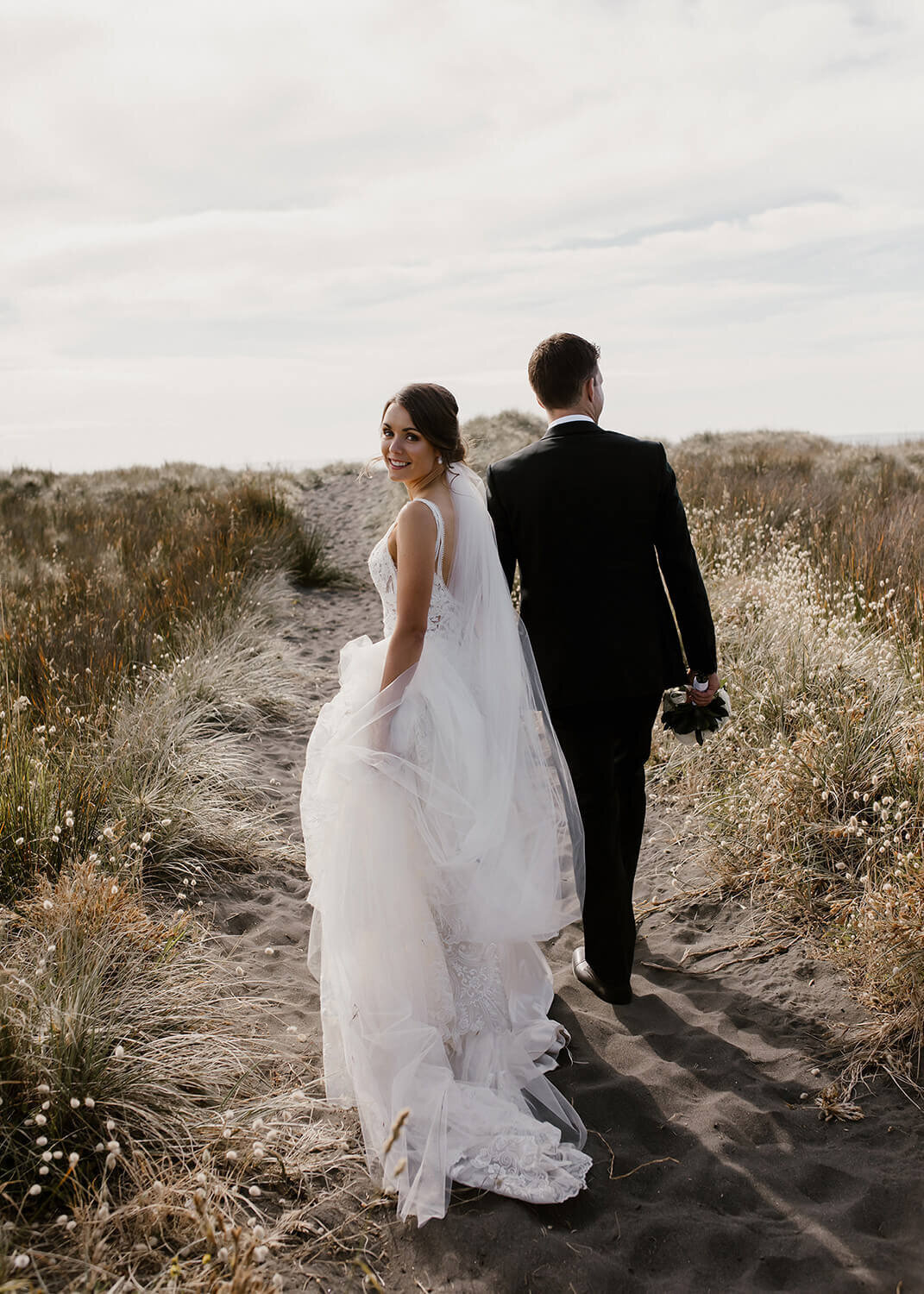 Aimee kelly photography photographing a bride and groom walking along a beach in new plymouth duirng their wedding photoshoot