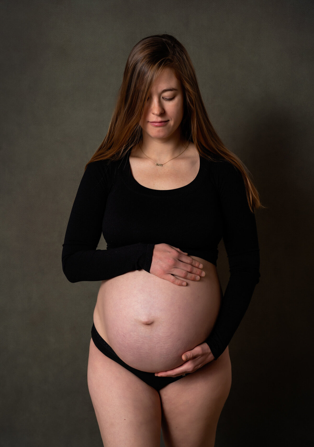 A mama in a black shirt cradles her baby bump during a portrait session with an Asheville Maternity Photographer