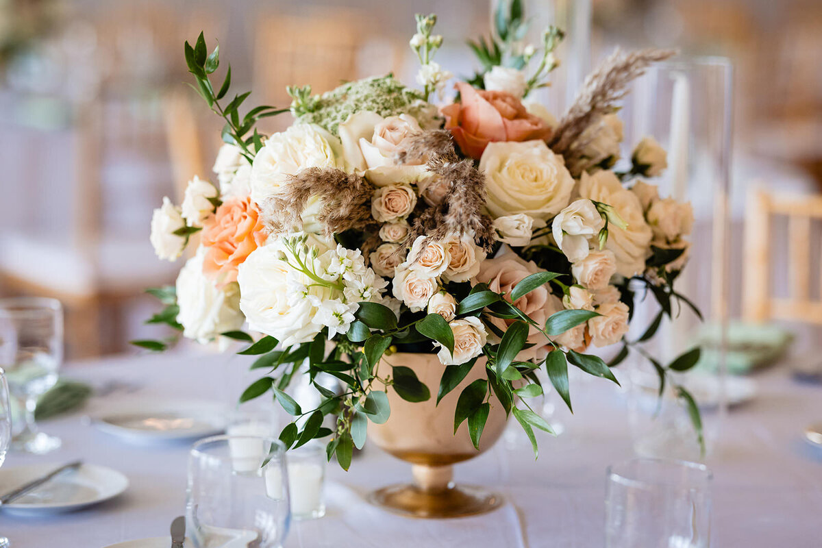 A lush floral centerpiece with white, orange, and green flowers set on a wedding reception table, complementing the elegant dinner setting.