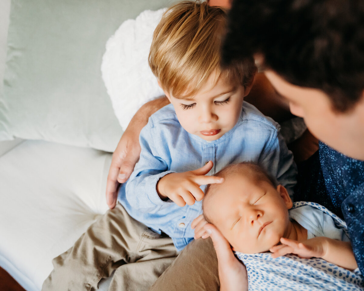 Newborn Photographer, dad holds baby as his older brother also admires him