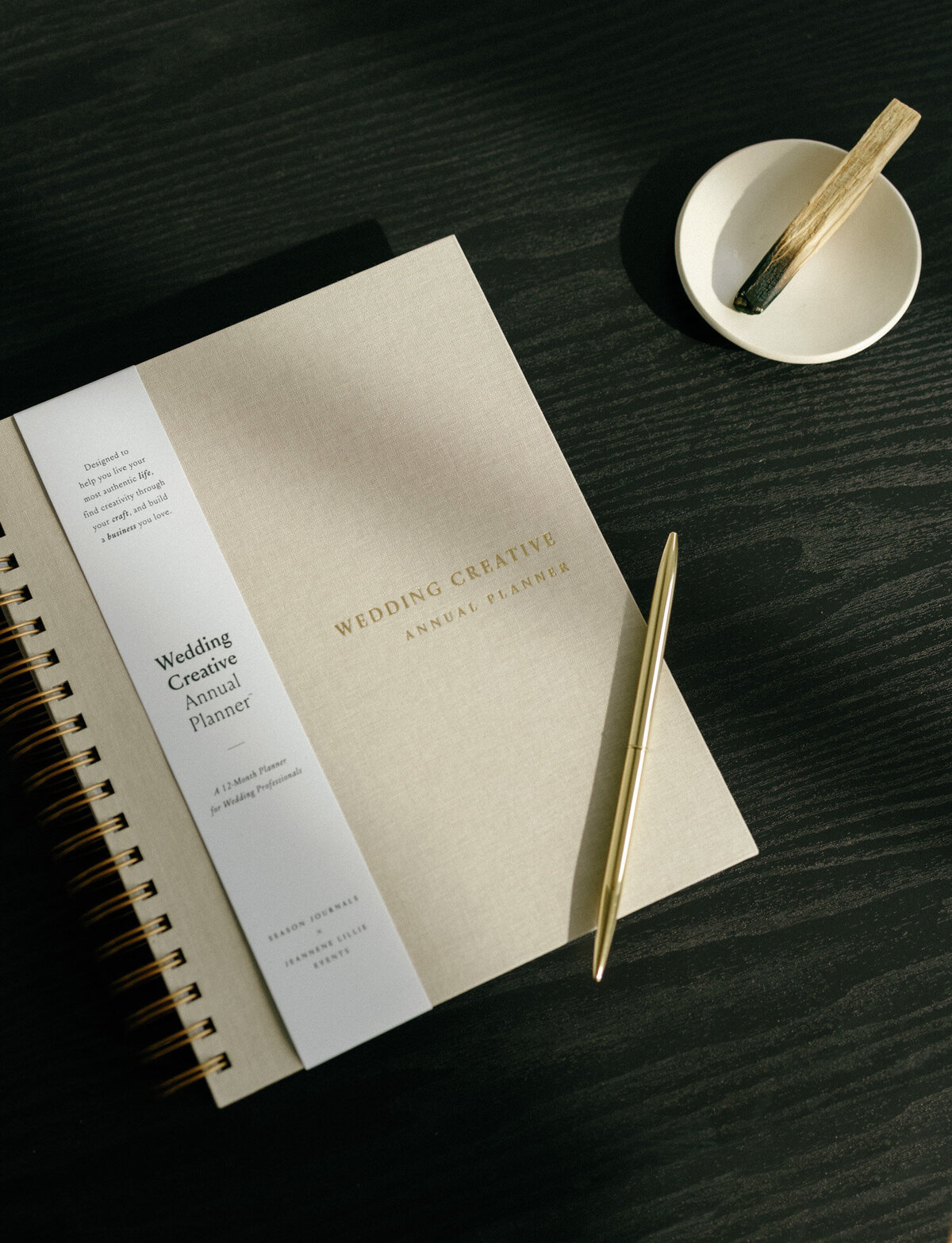 beige linen wedding creative annual planner with gold pen, gold lettering, palo santo on black table