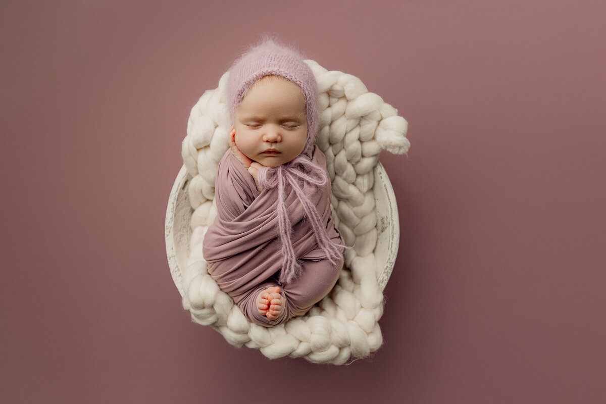 Baby girl sleeping peacefully in a pastel purple setup, styled with soft textures and wrapped in mauve for a cozy and modern studio look. Photographed by Inland Empire newborn photographer Kaitlyn Dawn.