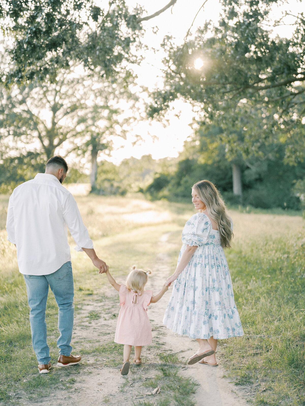 pregnant mom, daughter and father walking in field at sunset