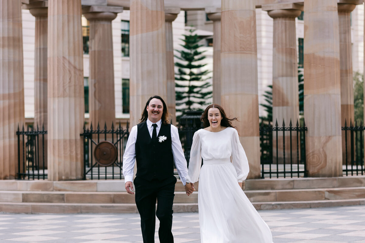 Joyful bride and groom walking and laughing together at Anzac Square in Brisbane after their registry office wedding.