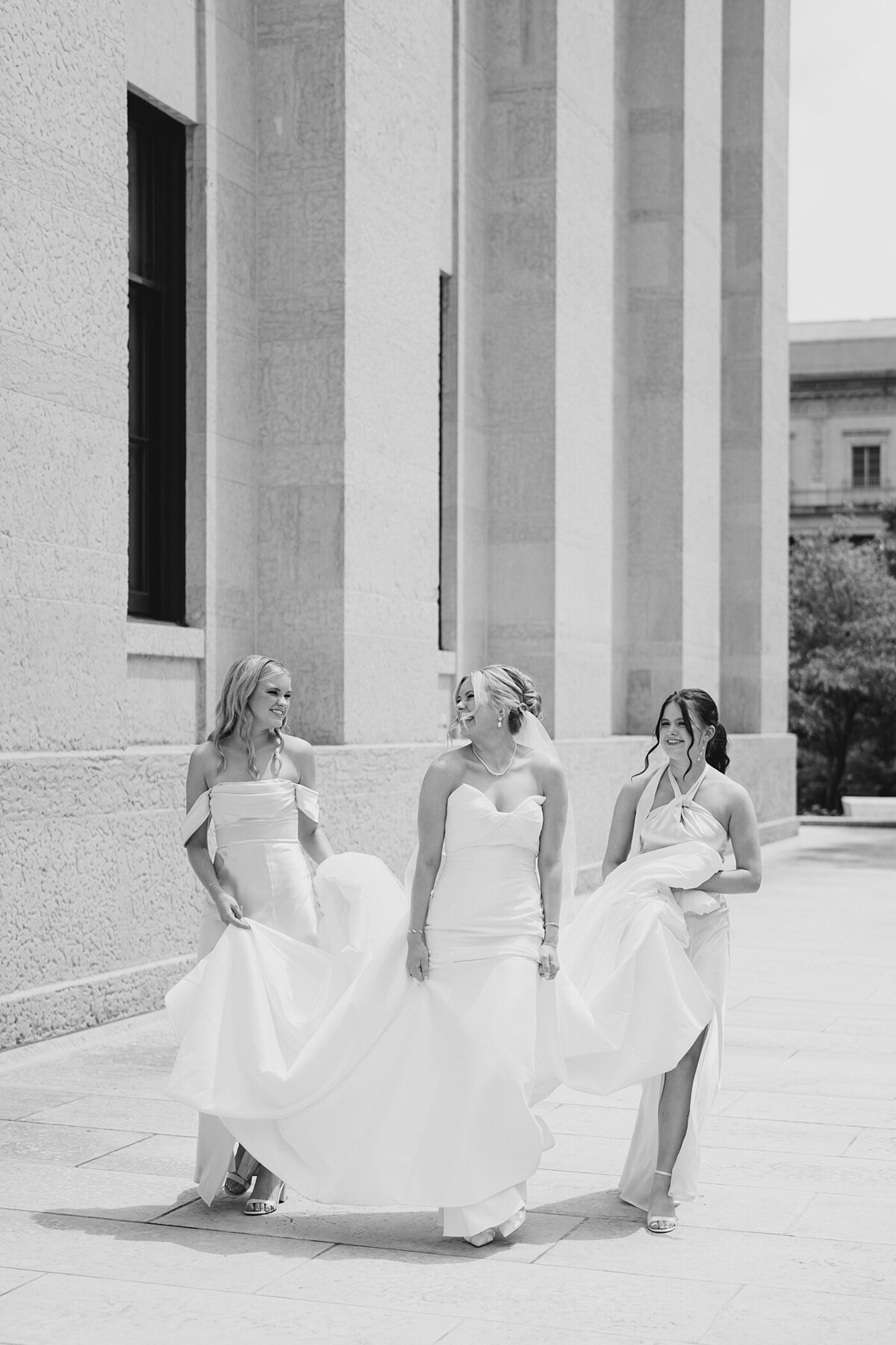 Columbus wedding  photographer captures bride walking with two bridesmaids holding her gown