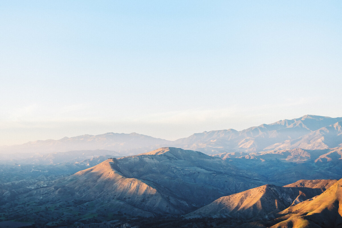 Dramatic sunset view of the Santa Ynez Mountains in Santa Barbara, California. Golden hour landscape photography showcasing the rugged coastal mountain range with soft pastel sky. Architectural peaks and valleys cast in dramatic light and shadow. Perfect backdrop for luxury Santa Barbara weddings and elopements.