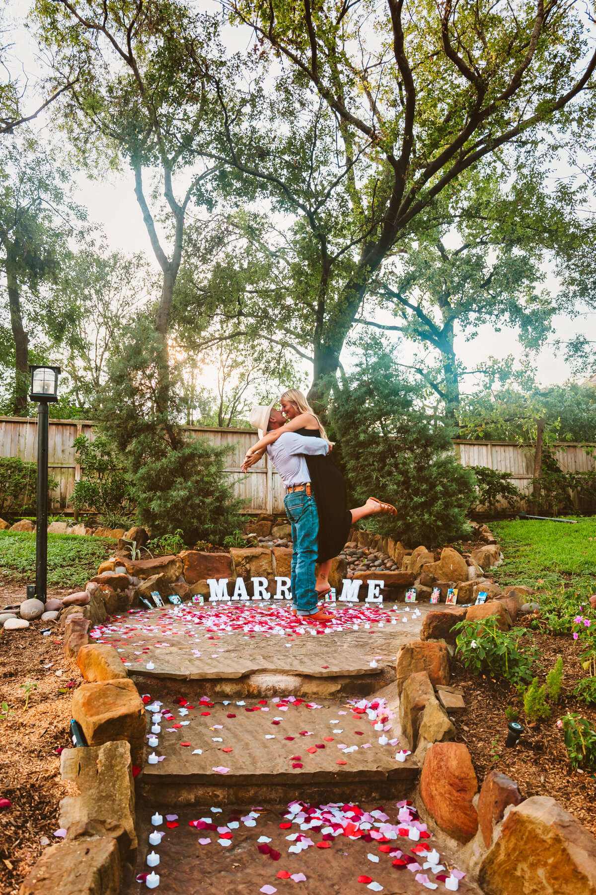 A joyful embrace following a successful proposal at The Rainbow Lounge in Houston, Texas. The couple hugs among rose petals with a “Marry Me” sign in the background. 