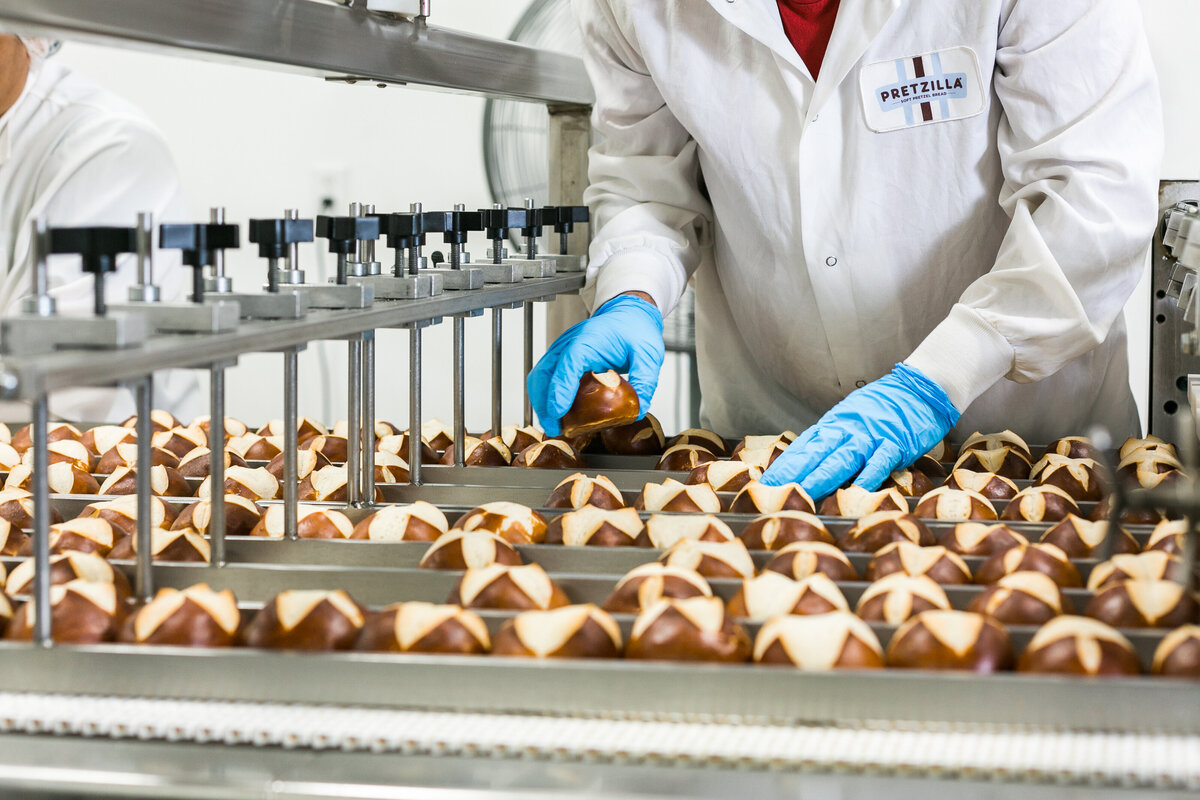 employee wearing a white coat and gloves sorting pretzel buns on a production line in a manufacturing and industrial setting
