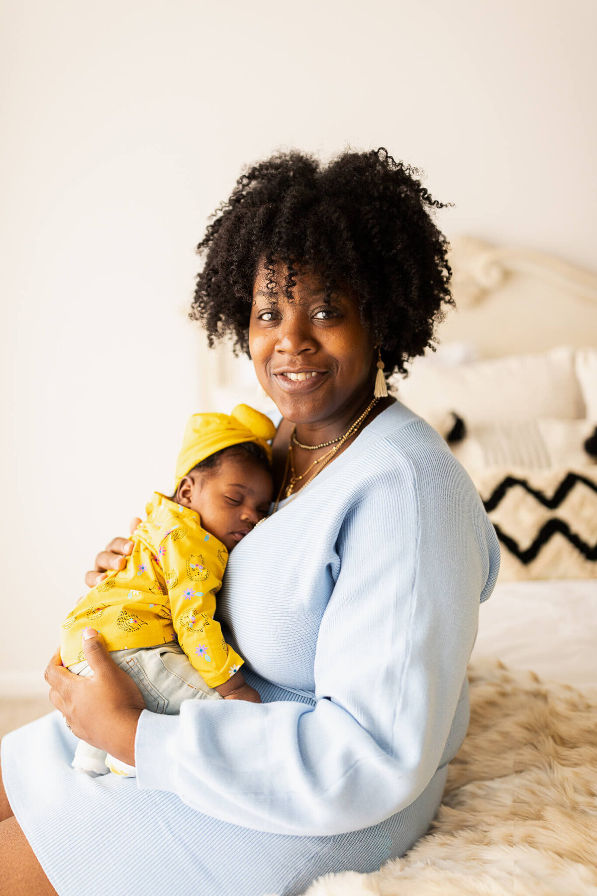 Mom in blue dress sitting on a bed holding her newborn baby girl