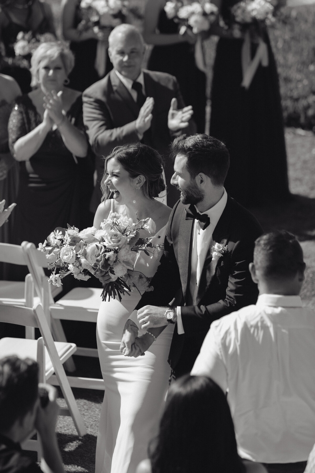 Bride and groom exiting ceremony aisle, guests applauding, authentic candid wedding moment in La Jolla.