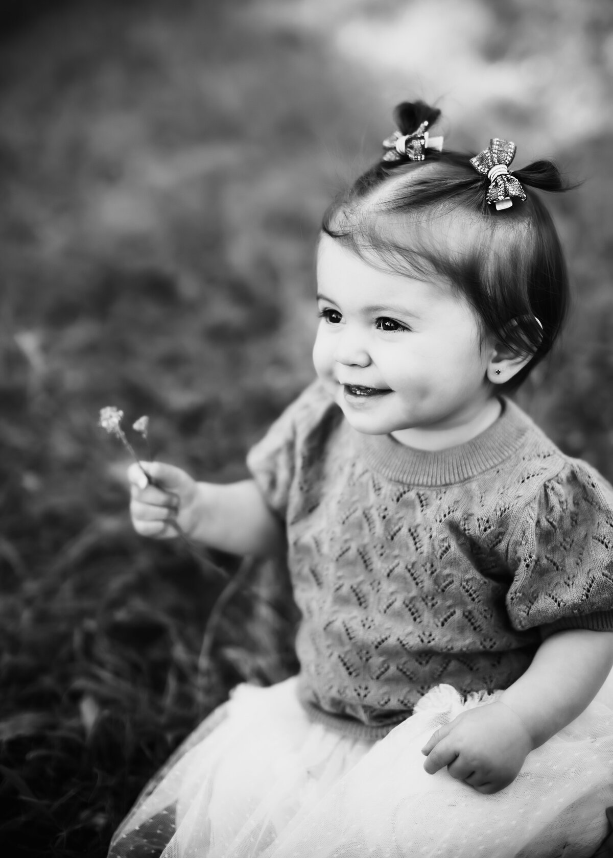 sweet black and white photo of toddler smiling and holding a flower in a field in Denver Colorado for family photography session
