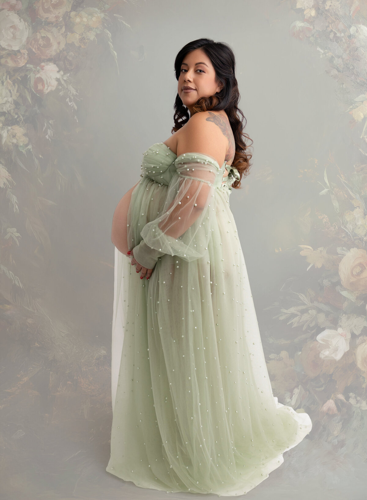 A pregnant mom wearing an elegant soft green colored gown with pearls stitched on the dress.