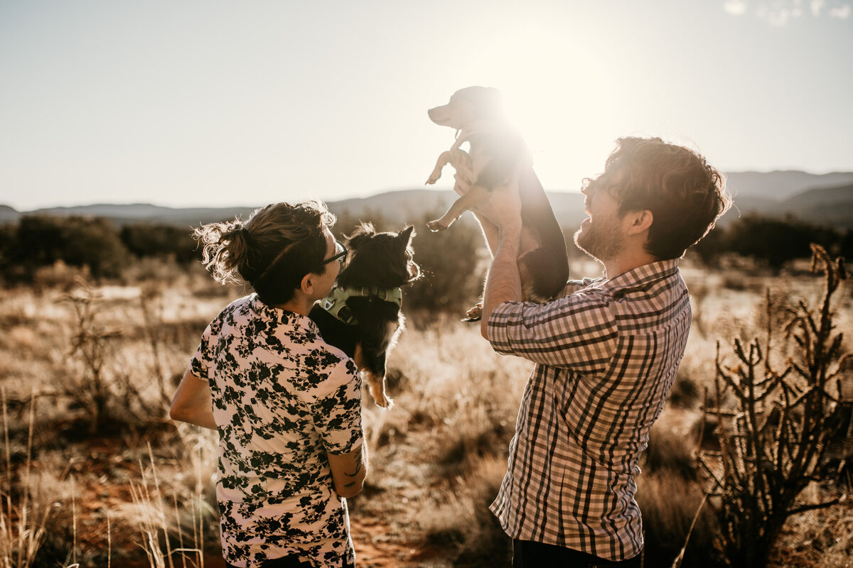 same sex couple holding up dogs in desert