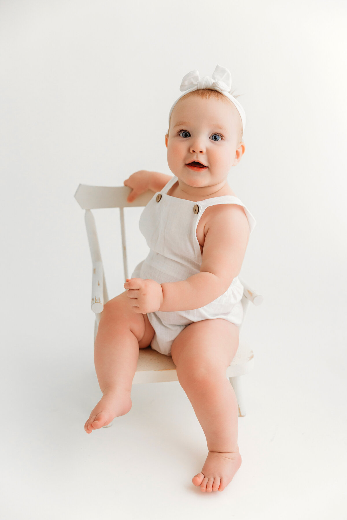 baby girl smiling in white chair in white outfit in phoenix milestone session