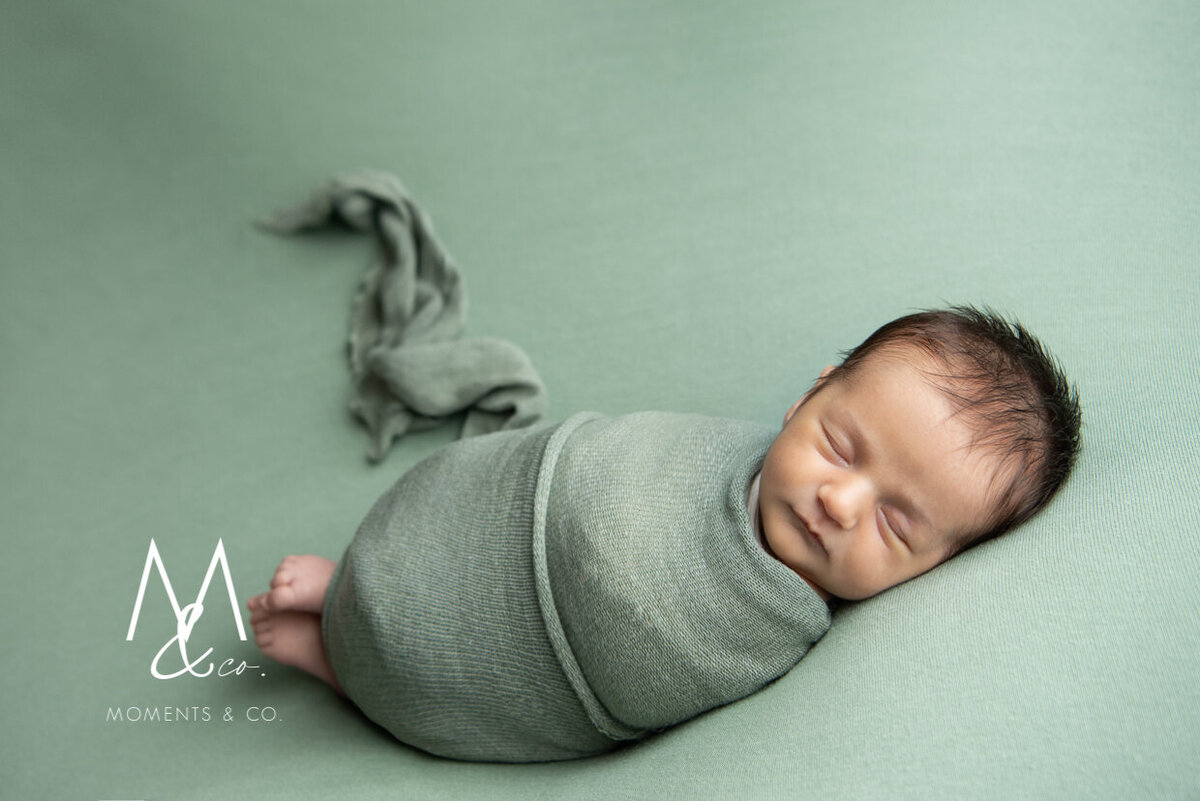 Newborn-Girl-in-coming-home-outfit-wrapped-on-green-blanket-photo-2