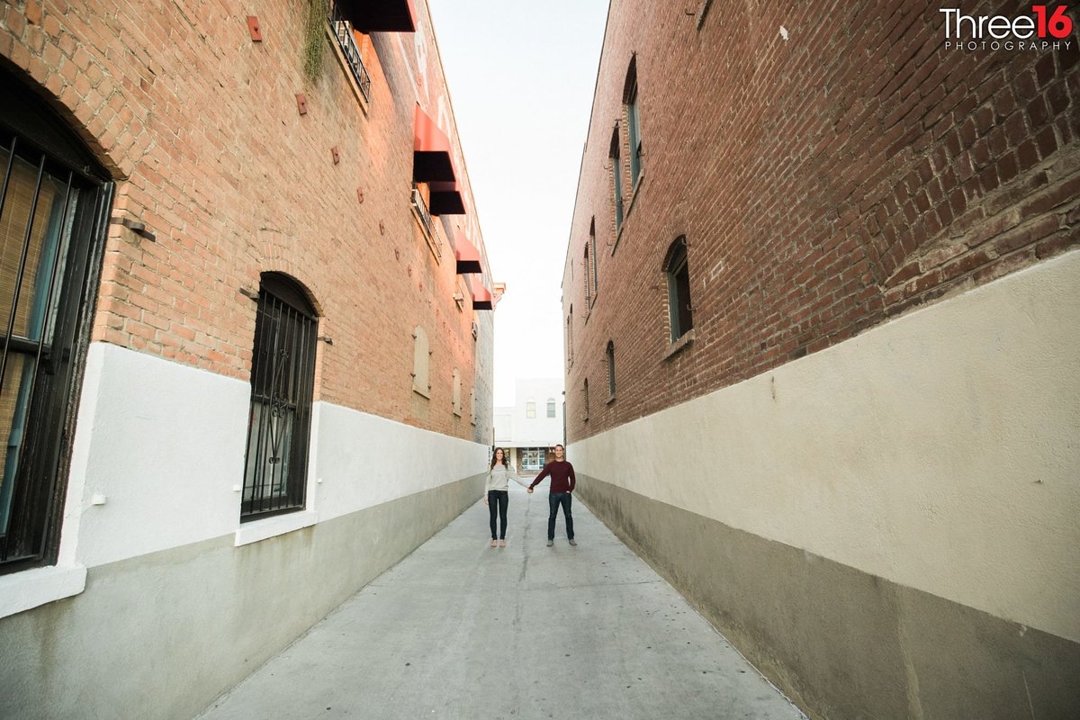Engaged couple hold hands in an alleyway during engagement photo session
