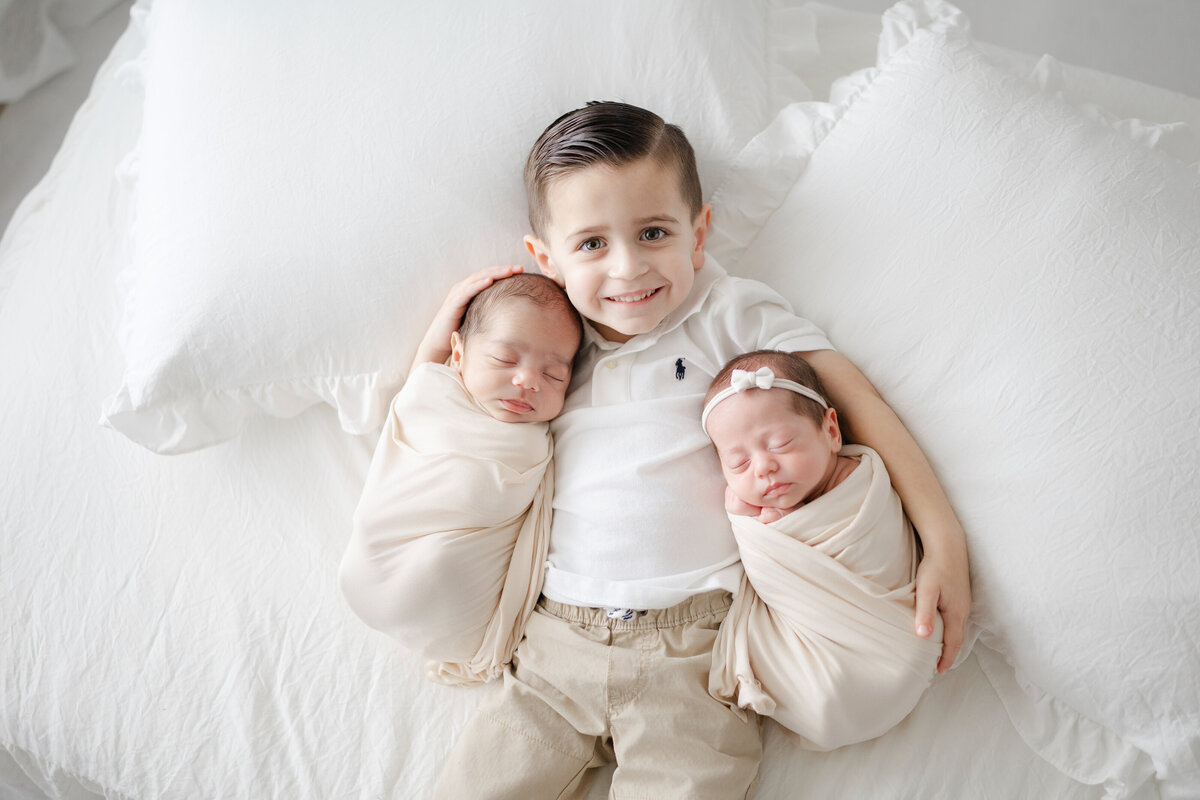 Luxury newborn portrait with big sister cuddling baby brother in soft neutral studio setting in Tampa