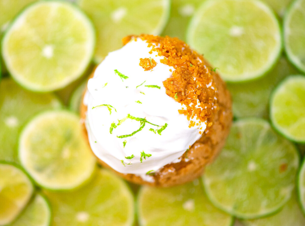 Handcrafted cream puff topped with icing, surrounded by sliced limes and strawberries, created by Crème Cream Puffs, playful and modern cakes & desserts in Calgary, Alberta, featured on the Brontë Bride Vendor Guide.