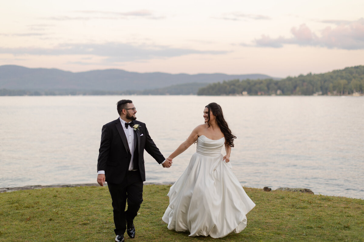 Bride and groom run through the grass, with the lake and mountains behind them