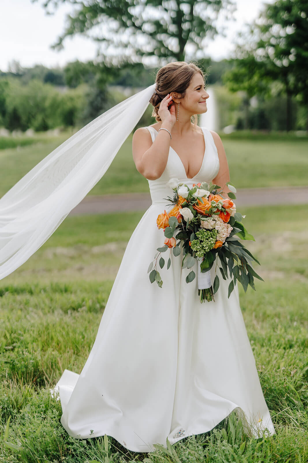 Bride with long veil stretched out standing in field at Oswego wedding, NY