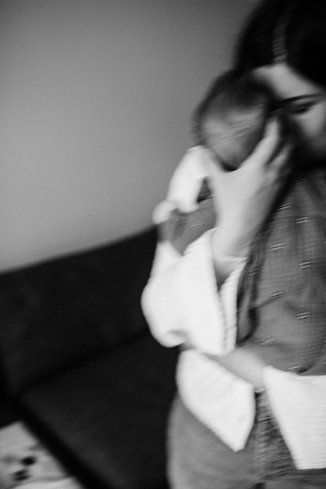 Blurred black and white image of a person holding a baby, captured by a Toronto in-home family photographer, standing in front of a couch.