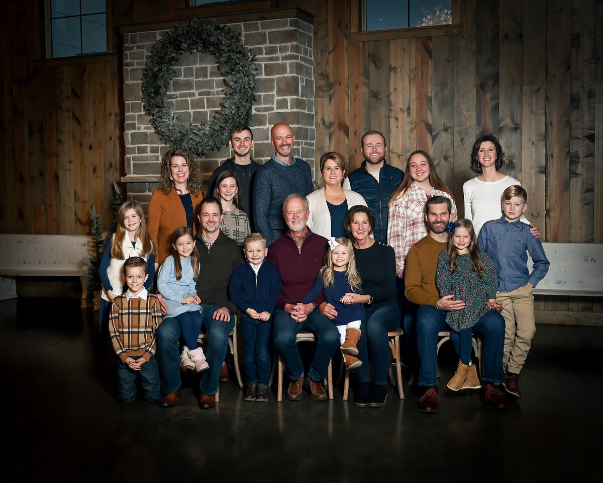 Large family poses in front of a rustic wood wall and fireplace