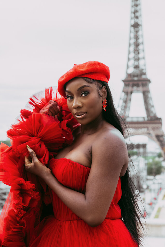 Elegant Paris portrait featuring black woman holding red dress train and matching beret with Eiffel Tower view