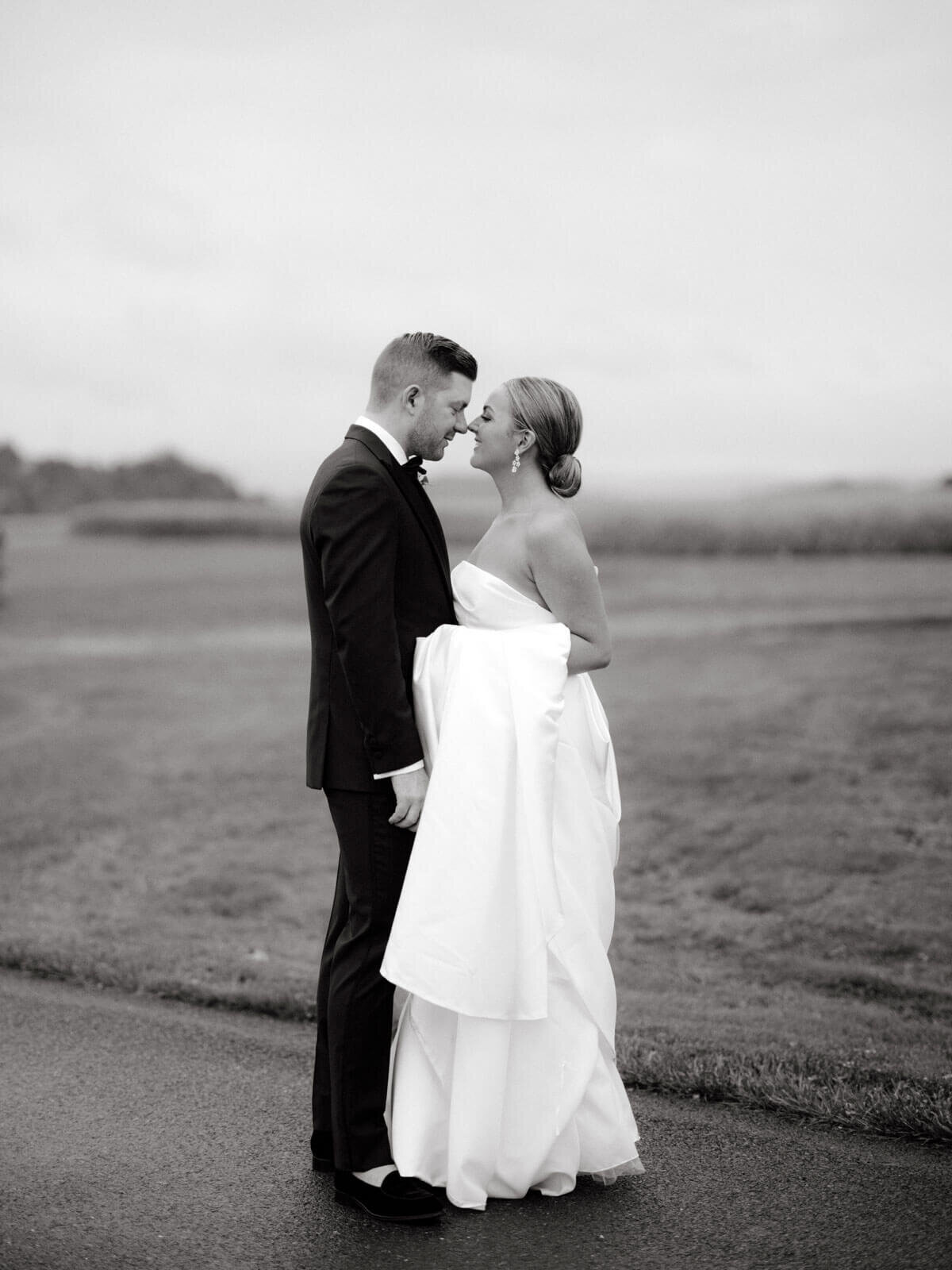 The bride and groom are standing close, nose touching, outdoors at Lion Rock Farm, Sharon, CT.  Image by Jenny Fu Studio