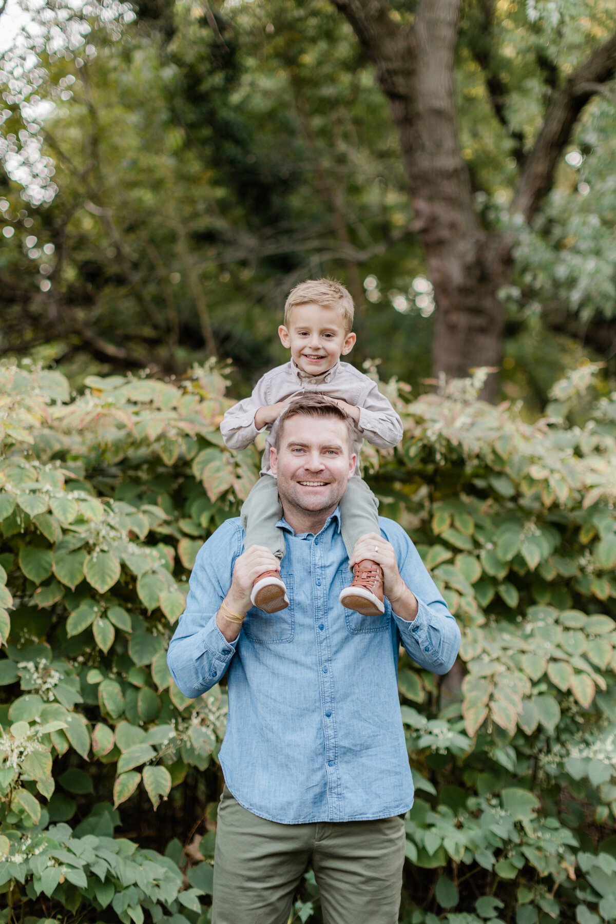 Father holding his son on his shoulders in front of lush greenery photographed by Family Photographer South Jersey Tara Federico