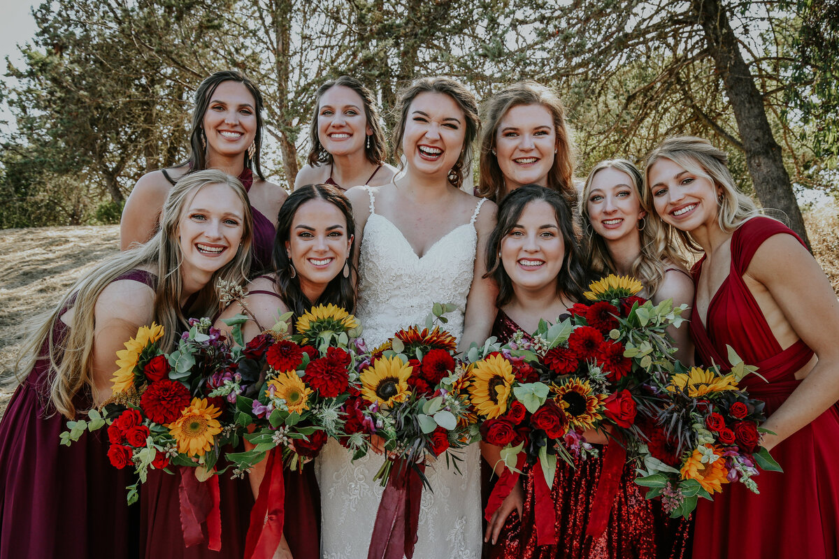Bride smiles at camera with bridesmaids while they hold bouquets.
