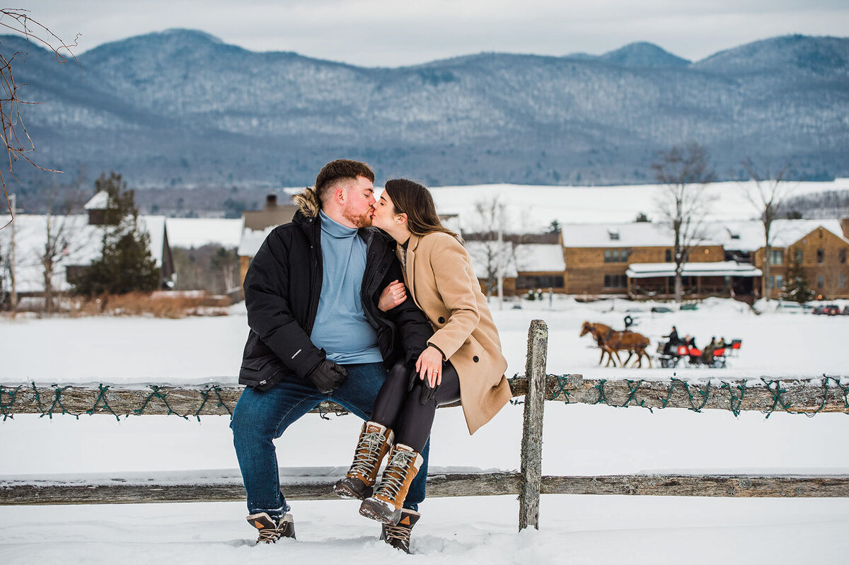 couple sitting on fence with sleigh ride in winter mountain top inn