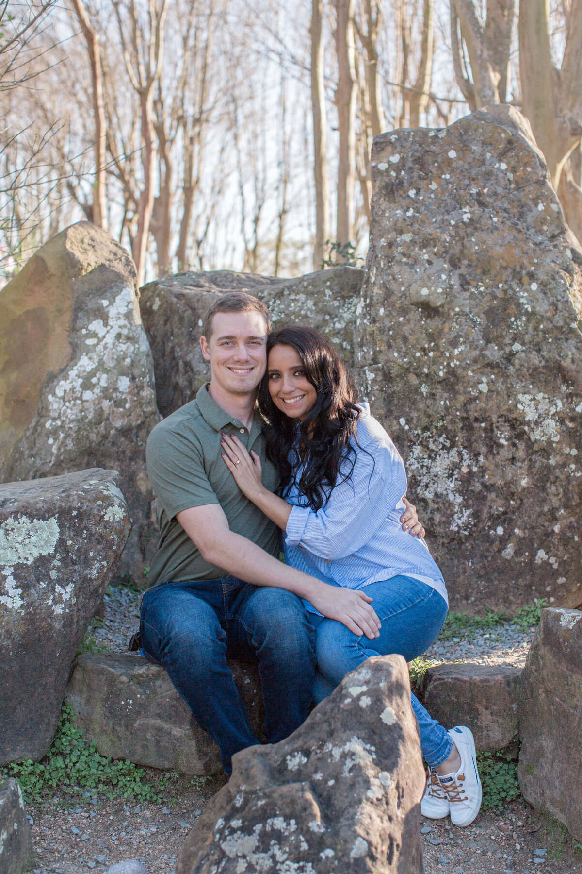 A couple smile for the camera while seated on a rock outcropping just after their surprise engagement. Boulder engagement photography by Stephanie Eddy