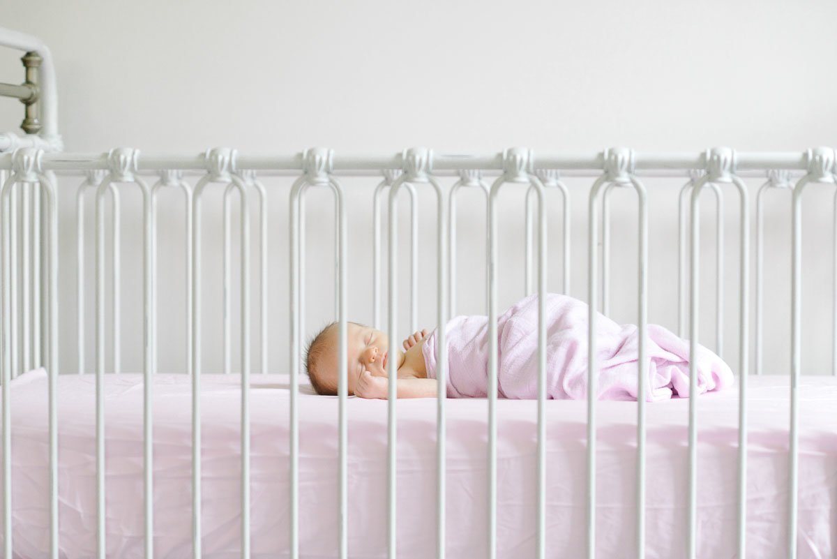 baby girl sleeping in white iron crib on pink mattress