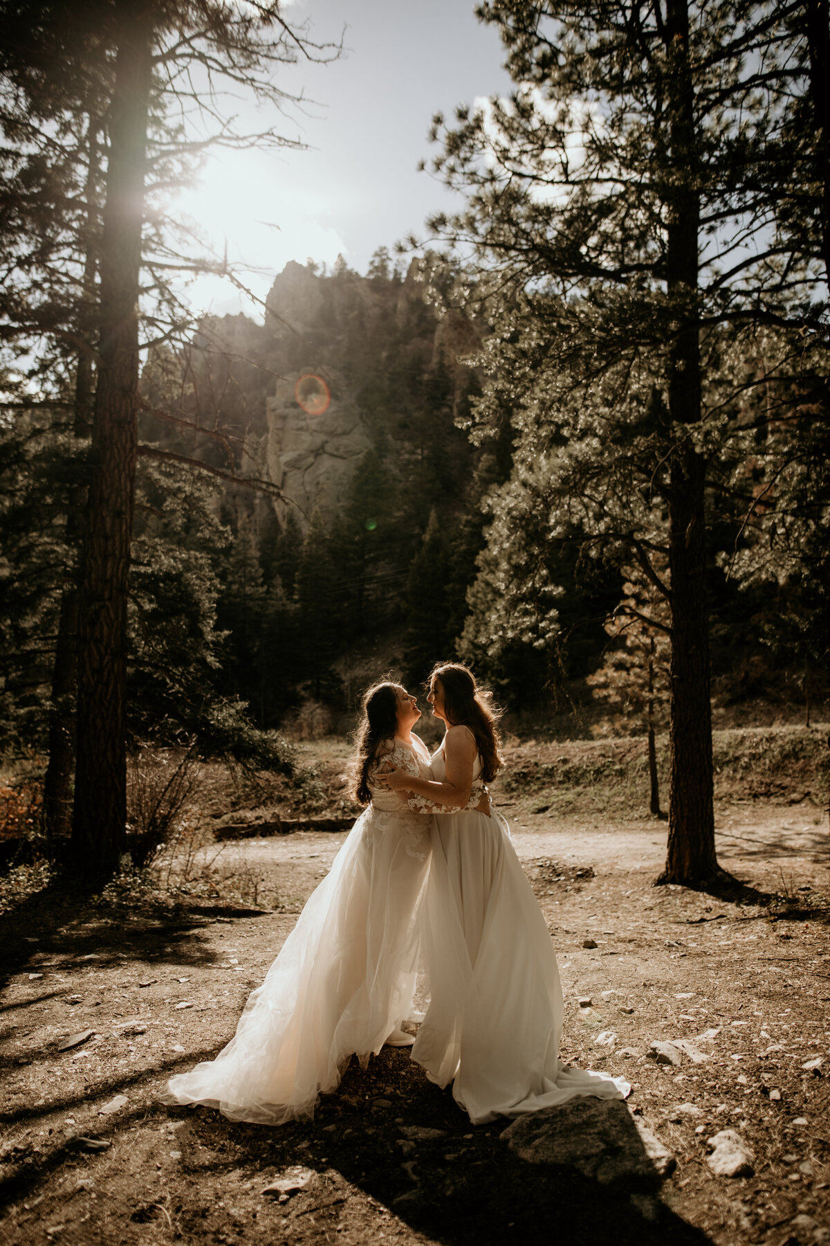 same sex female couple holding each other in bridal gowns with sun behind them