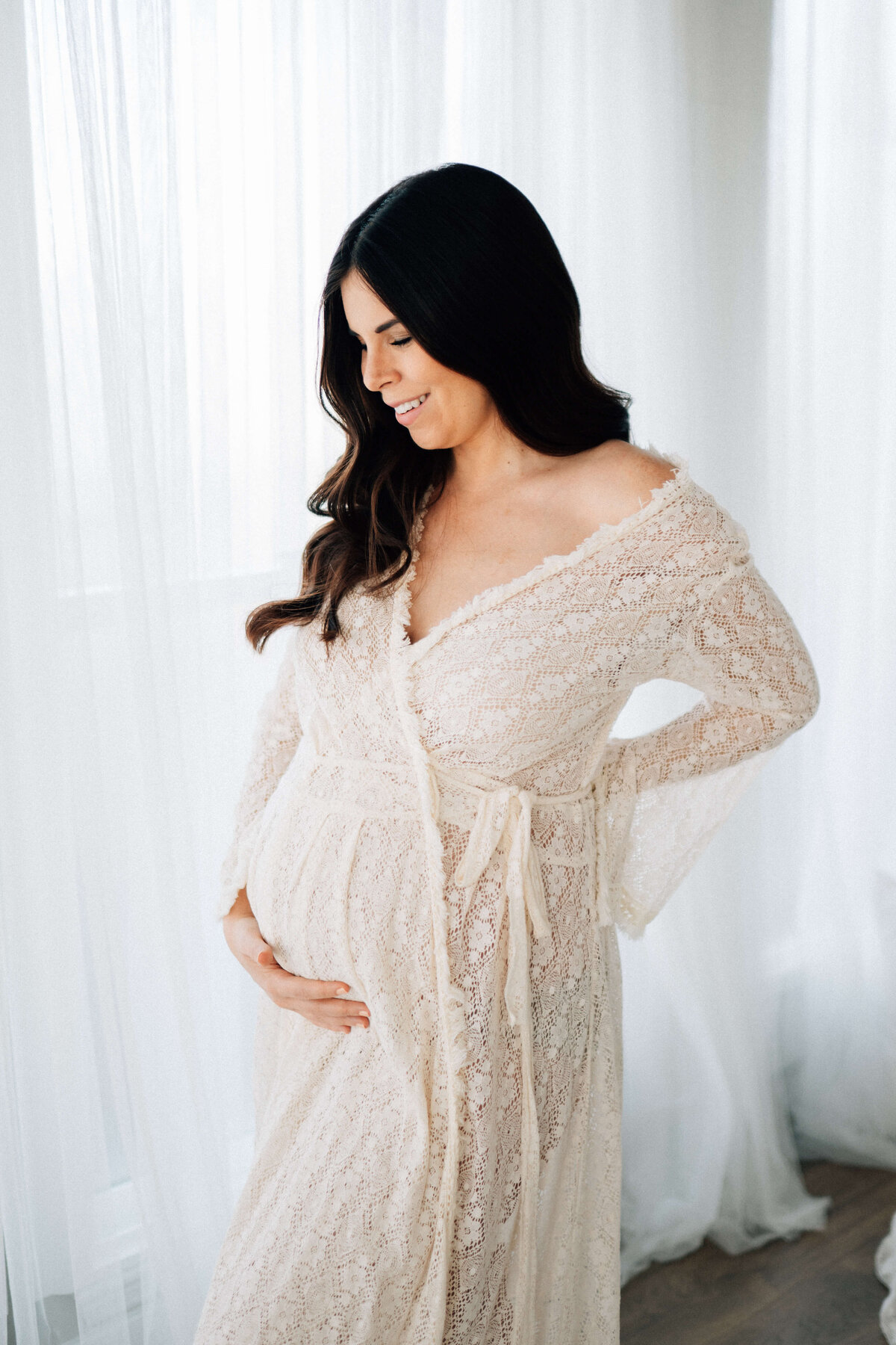 maternity mother holding her belly  in front of a window