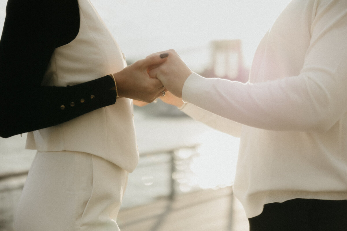 Man and woman holding hands with the Brooklyn Bridge glowing in the background behind them in New York City, NY, by Andrea-Marie Photography