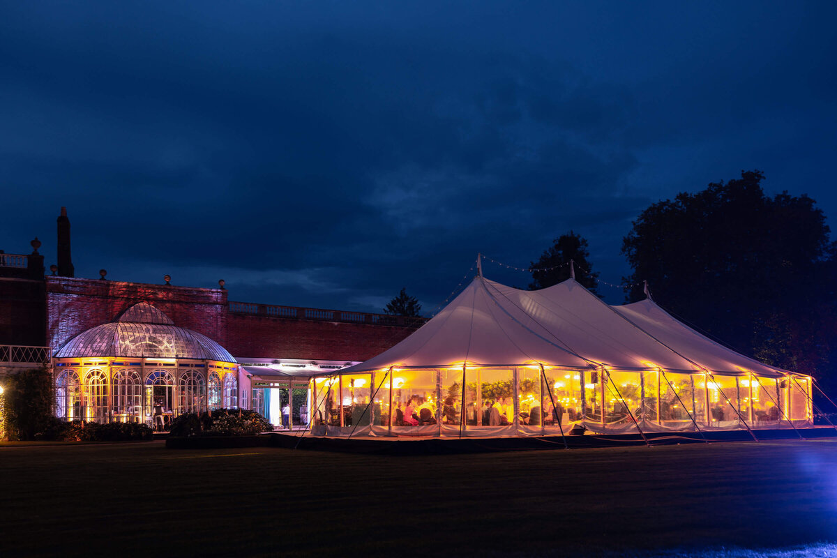 a canvas event marquee in the grounds of avington park lit up with golden lighting at night for a luxury 50th birthday party