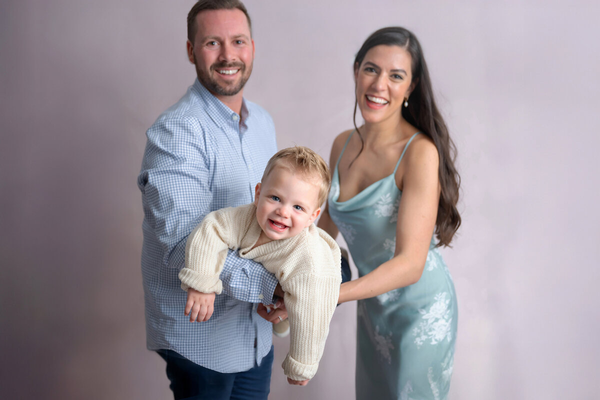 Man and woman holding a smiling child belly-down between them, with the child looking forward joyfully.