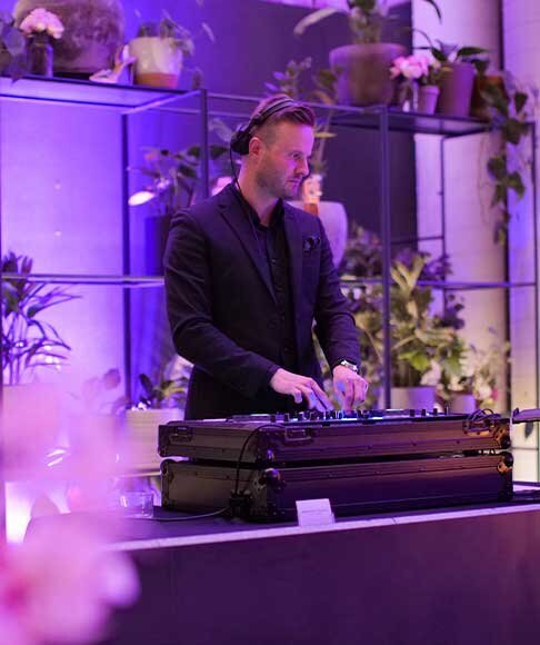 Male DJ playing at a high-end fashion launch event with purple lighting and indoor greenery