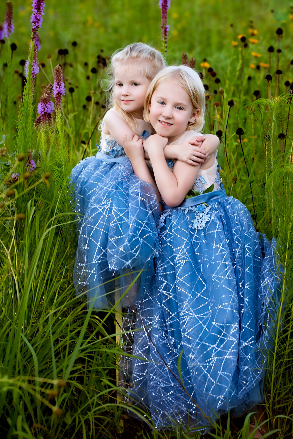 Beautiful portrait of two sisters in matching blue dresses, surrounded by vibrant wildflowers. Captured in Overland Park, Kansas, this vibrant and natural setup is ideal for families seeking creative sibling photography.