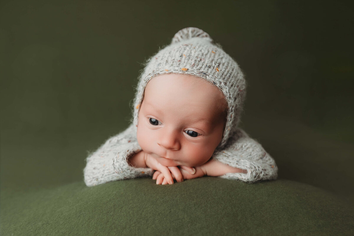 awake newborn boy in a grey fuzzy outfit with a matching bonnet on a green backdrop in his york newborn portraits 