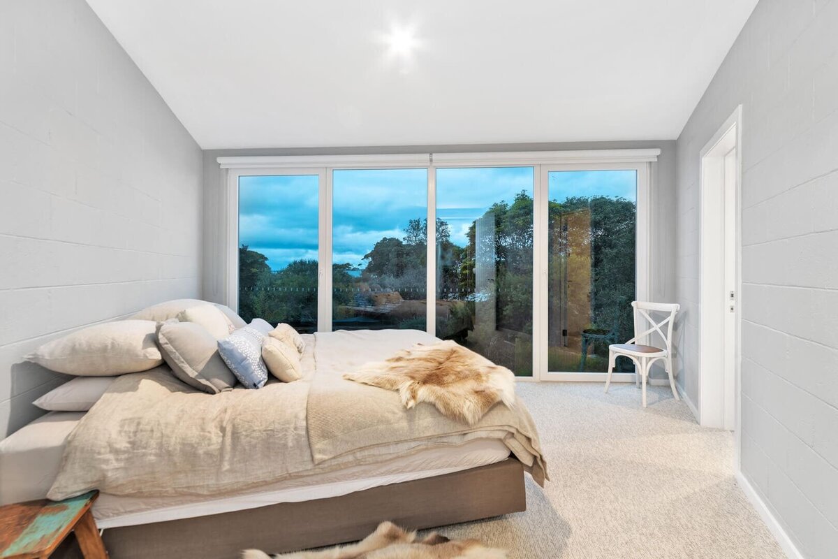 Bathroom with a wall as windows. Double bed in the middle of room with beige sheets