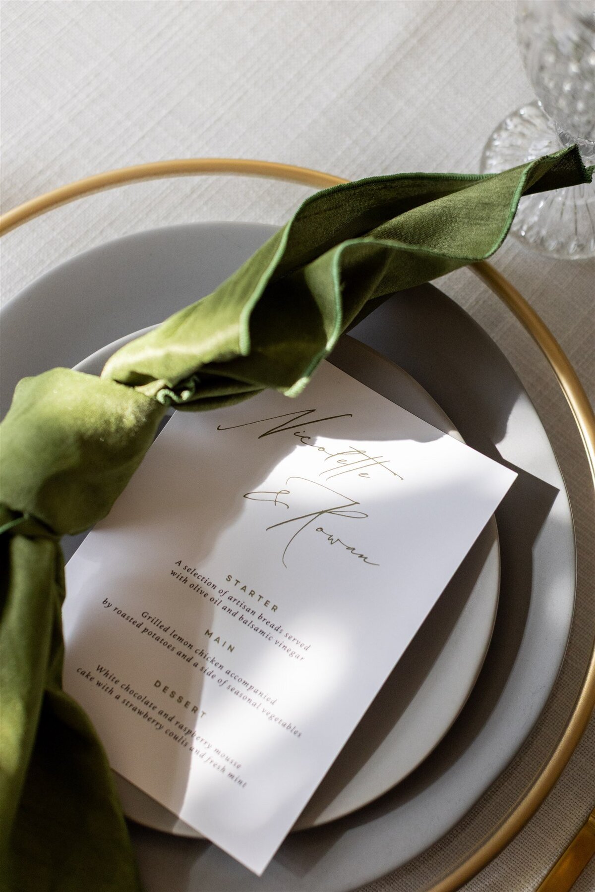 A table setting with a thoughtfully designed wedding menu and green linen napkin.