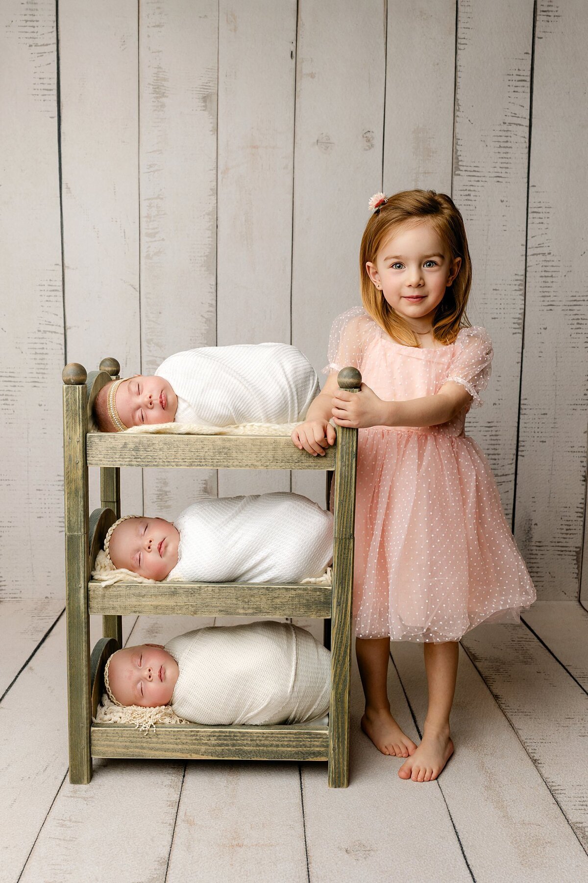 Three baby sisters posed on bed with big sister in the quad cities studio in Bettendorf iowa