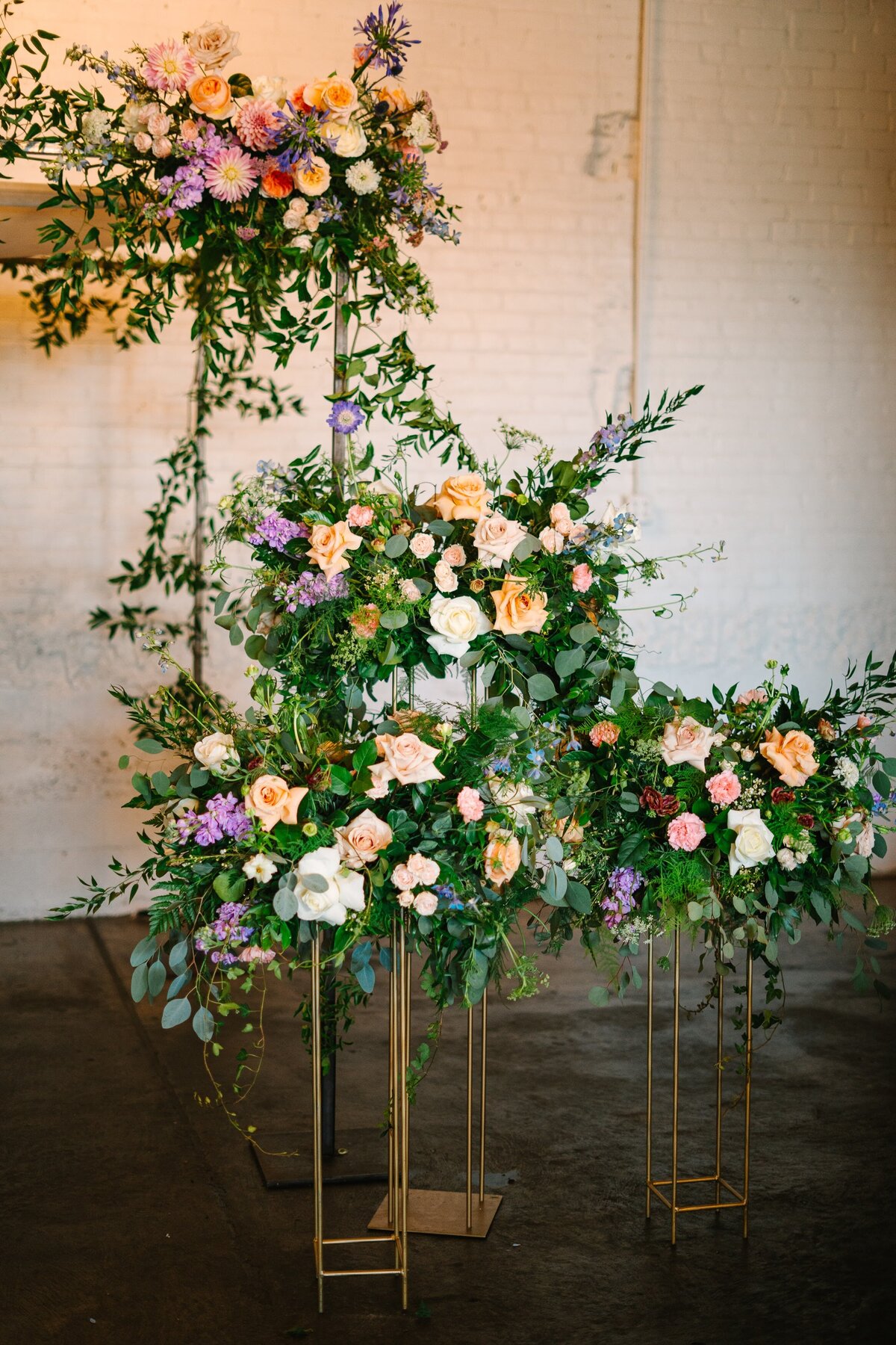 Purple, peach, and orange floral arrangements on gold stands.