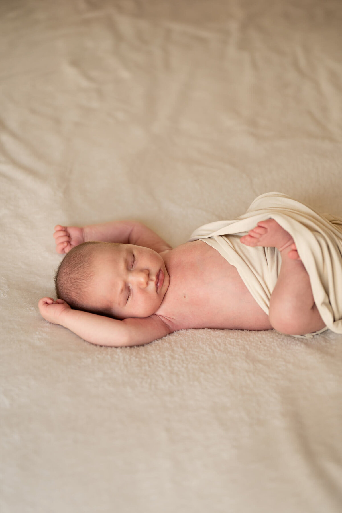 sleeping newborn with arms over head on a neutral blanket