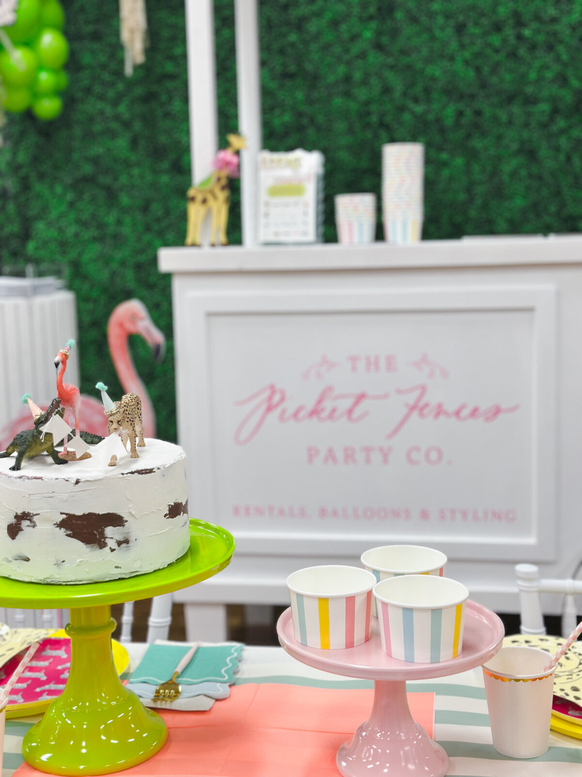 Decorated kids table with crocodile, cheetah, flamingo figurines, striped treat cups and party animal paper goods. 