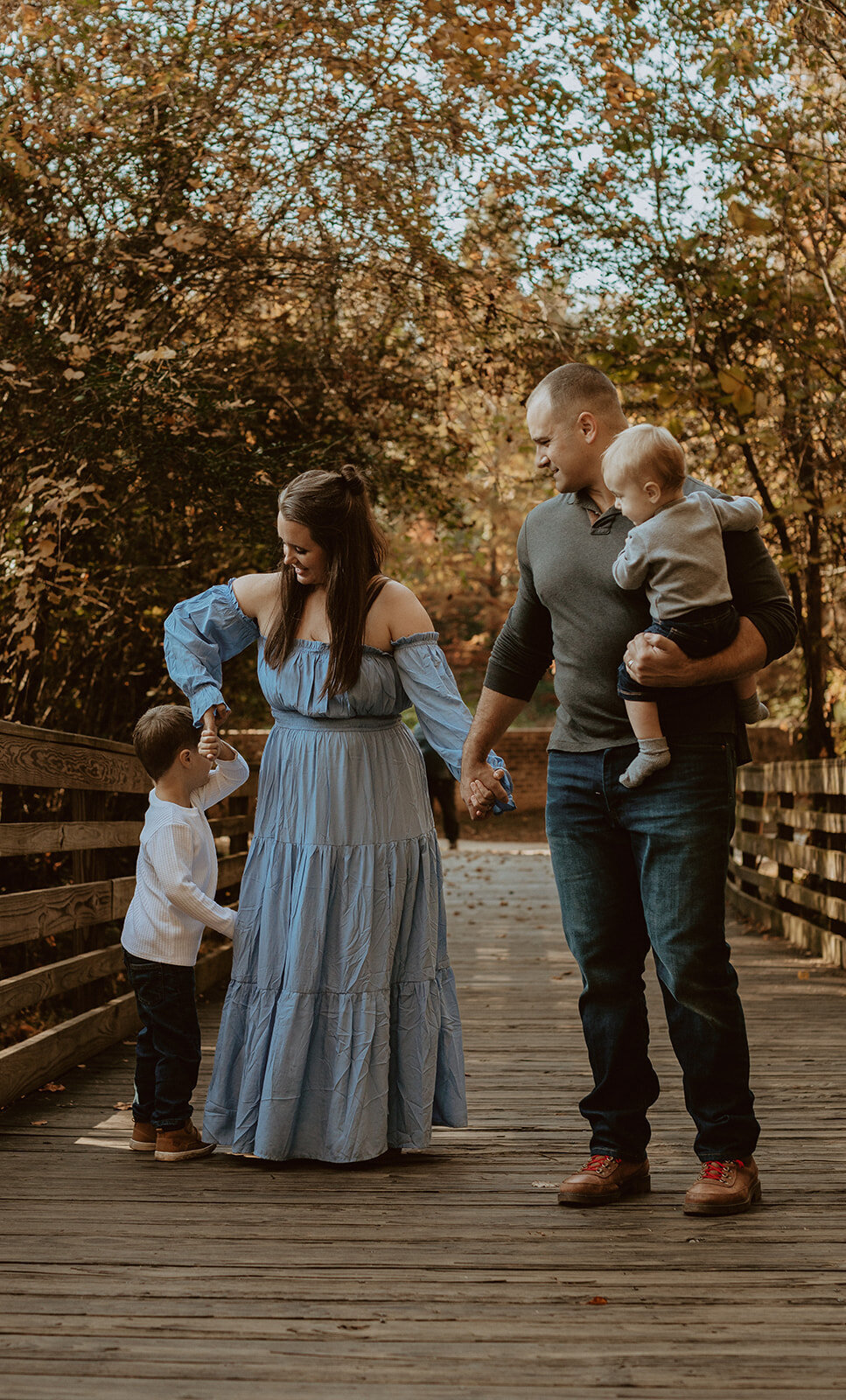 family of four walks across bridge with fall foliage